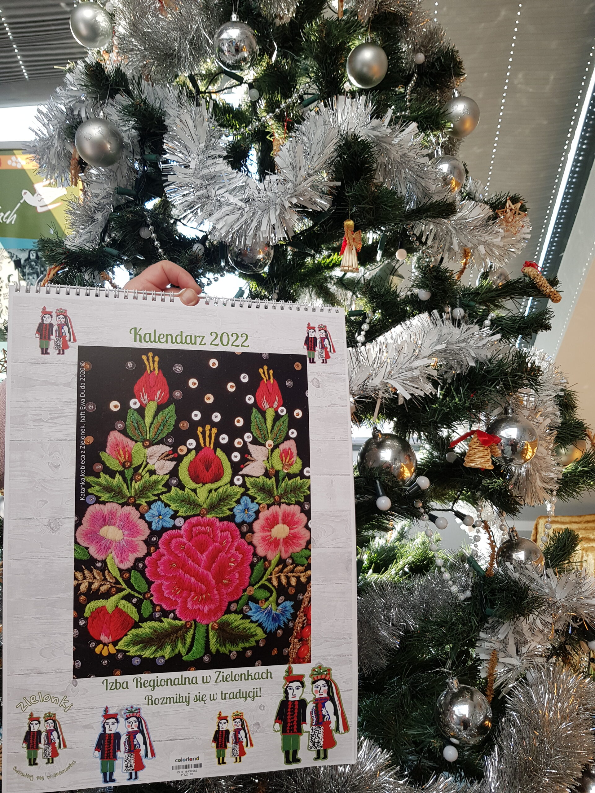 zdjęcie kalendarza na którym znajduje się wzór kwiatów z gorsetu krakowskiego, w tle choinka
