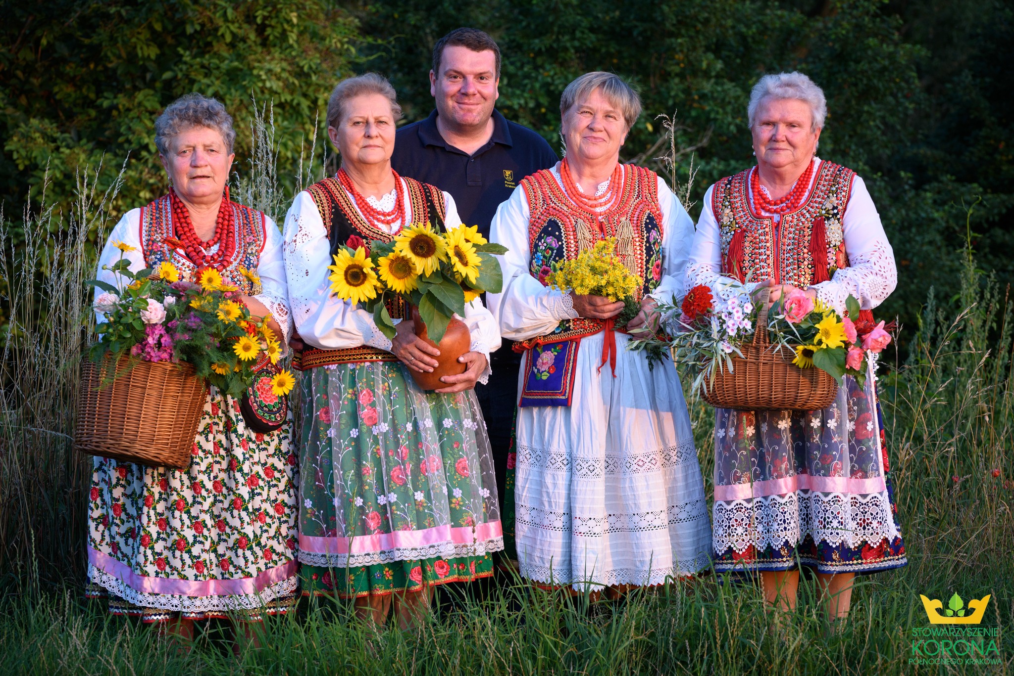 zdjęcie przedstawia cztery kobiety w strojach krakowskich i mężczyznę za nimi w plenerze