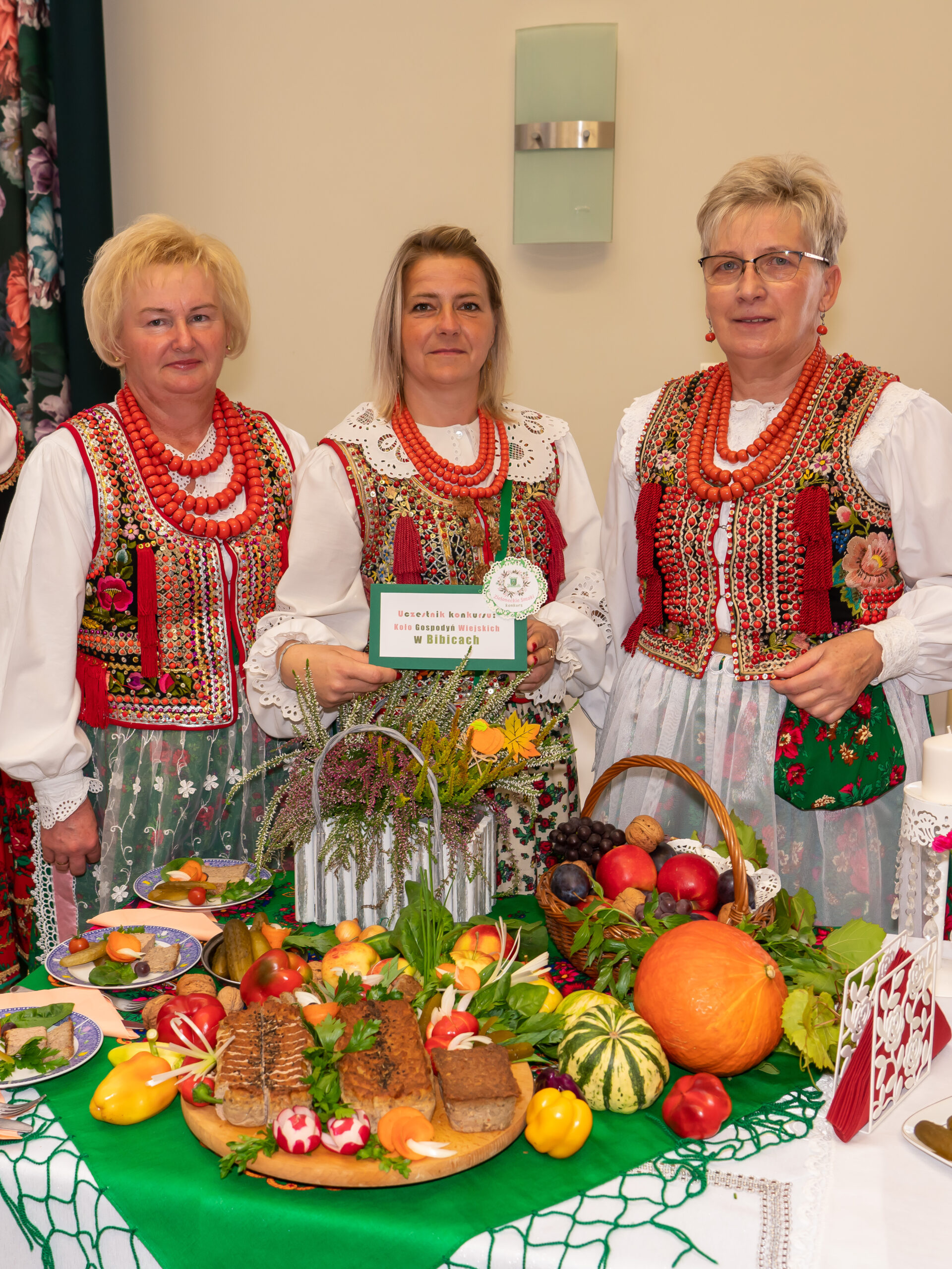 zdjęcie przedstawia trzy kobiety w strojach krakowskich przy stoliku z dekoracjami i jedzeniem